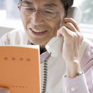 年金手帳を見ながら電話をかける高齢男性