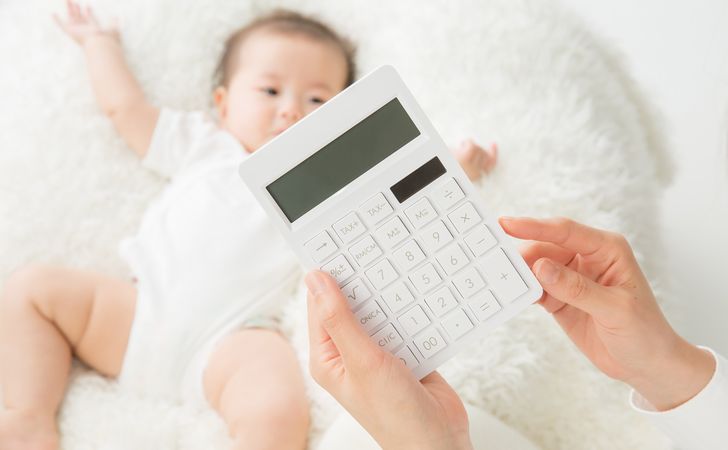 赤ちゃんの傍で計算機を持つ女性