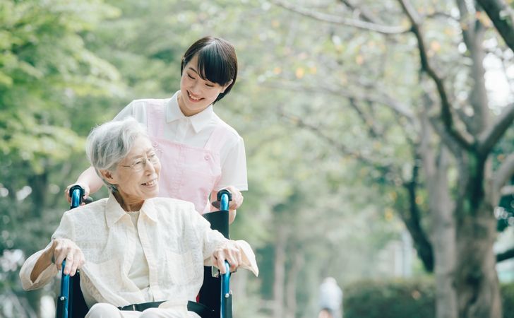 車椅子に座る高齢女性と、車椅子を押す介護士の女性