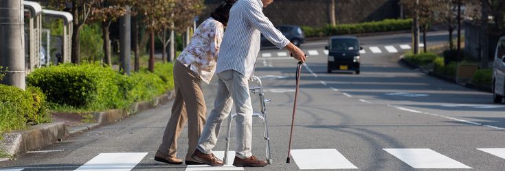 歩行補助具を使って歩く高齢女性と、杖をついて歩く高齢男性